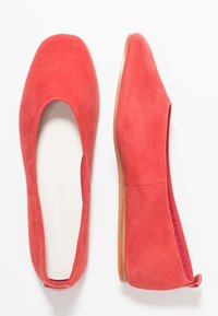 Ballerines en suede rouge avec un bout carré et un design minimaliste, présentant une doublure intérieure douce et une semelle plate et flexible.
