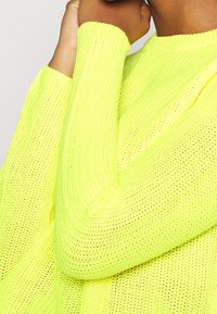 Jasnożółty sweter dzianinowy w neonowym kolorze, o luźnym, teksturowanym wzorze i szerokich mankietach, z otwartymi splotami dla lepszej wentylacji.