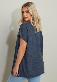 T-shirt blu navy, morbido e dalla vestibilità ampia, con scollatura rotonda e maniche corte. Tessuto morbido e texturizzato con spacchi laterali. Indossato con jeans in denim azzurro.