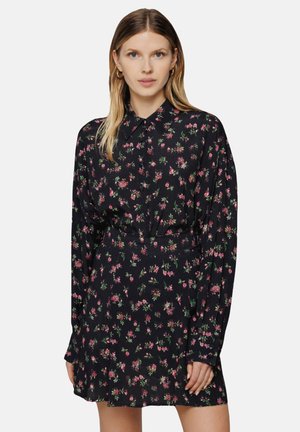 Schwarzes Blumenkleid mit langen Ärmeln, das einen Kragen und eine taillierte Taille hat. Kleine rosa und grüne Blumenmuster über das gesamte Kleid.