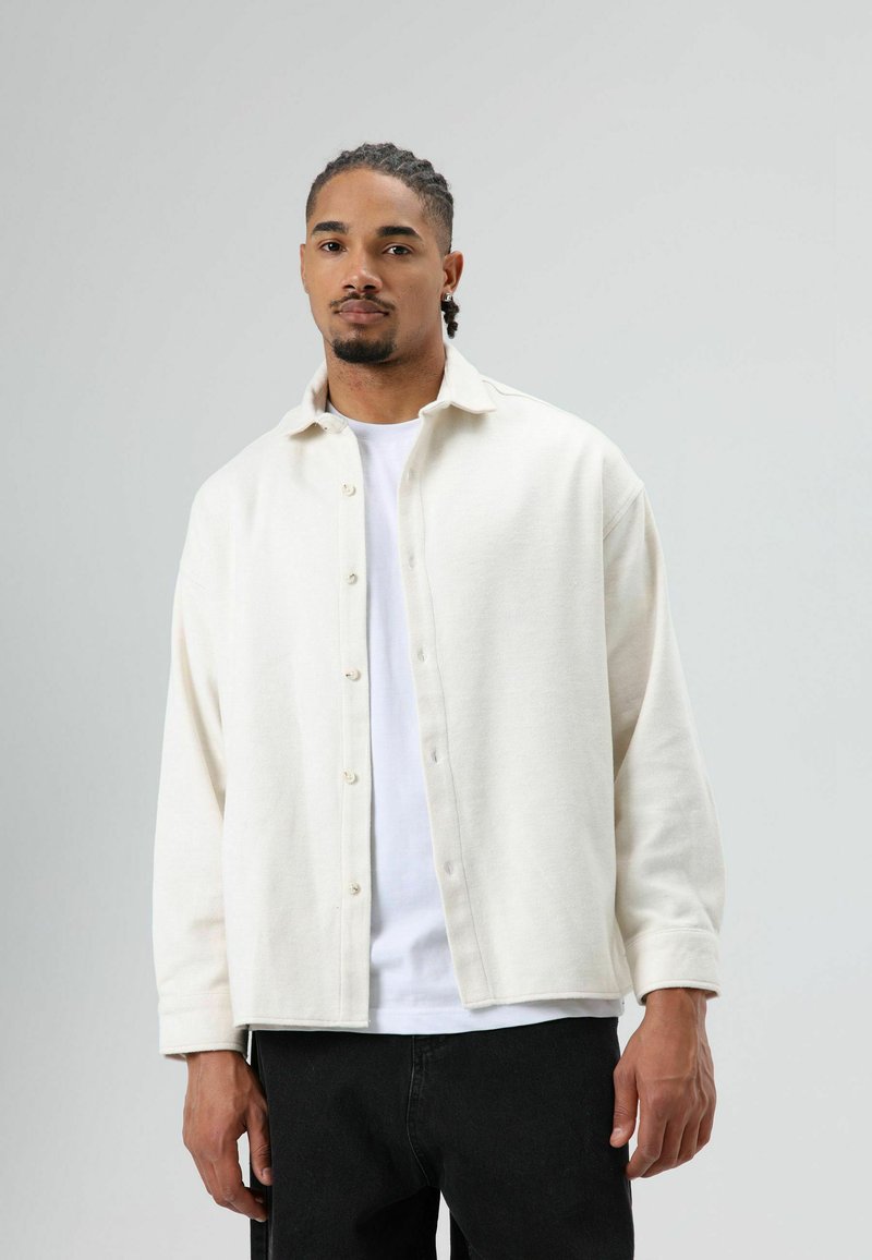 Lichtbeige overhemd met knopen, gemaakt van een zachte stof, met een kraag, lange mouwen en een losse pasvorm, gecombineerd met een witte T-shirt eronder.