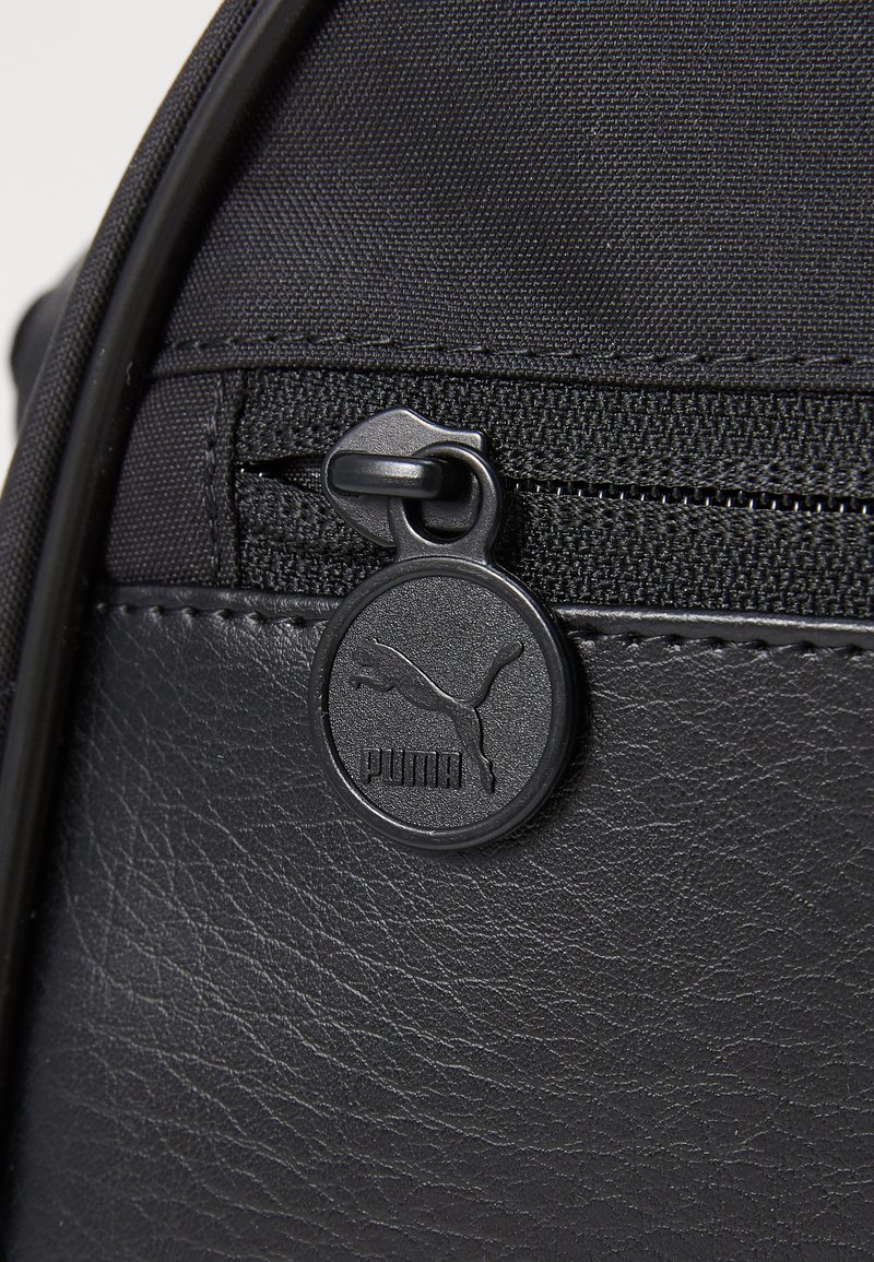 Zaino nero con un tessuto testurizzato e una sezione in pelle liscia, dotato di una zip rotonda nera con il logo Puma.