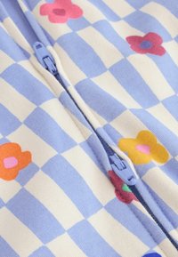Tissu à carreaux bleu clair et blanc avec des imprimés floraux colorés et une fermeture éclair bleu clair au centre.