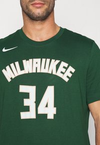 Zelené tričko s nápisem "MILWAUKEE" bílým písmem nad číslem "34" s texturovaným povrchem. Logo Nike na levém rameni.