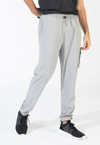 Grijze sportieve broek met een elastische tailleband, verstelbare trekkoord, taps toelopende boorden en details van zijzakken. Draagt met zwarte sneakers.