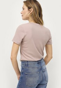 Maglietta rosa chiaro a coste con maniche corte, abbinata a jeans blu a vita alta con tasche posteriori visibili e un lavaggio sbiadito.