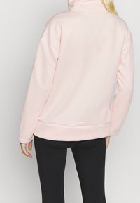 Pull-over rose pâle texturé avec col montant et accents blancs, conçu pour le confort. Il présente un logo à l'ourlet et une coupe ample.