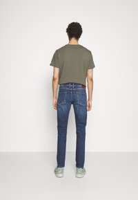 Mörkgrön kortärmad t-shirt för män i kombination med mörkblå slim fit-jeans. Jeansen har en läderlapp på bakre midjebandet.