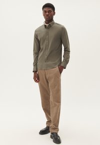 Olíva zöld, slim fit gombos ing, világosbarna kordbársony nadrággal és fekete bőr cipővel párosítva. Sima textúra és klasszikus dizájn.