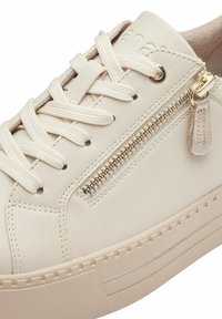 Fehér bőr sportcipő lapos fűzővel, oldalsó cipzárral, texturált részletekkel és varrott gumitalppal. Az alján egy diszkrét fémes csík található.