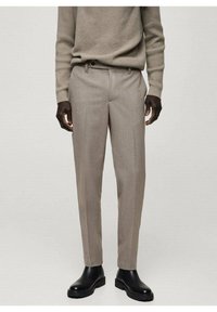 Beige op maat gemaakte broeken met een subtiele structuur, voorzien van een gladde voorkant, minimale zakken en een slim fit, gecombineerd met zwarte enkellaarsjes.