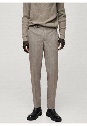 Pantalones tailored en color beige con una textura suave, presentan un frontal liso, bolsillos mínimos y un ajuste slim, combinados con botas negras hasta el tobillo.