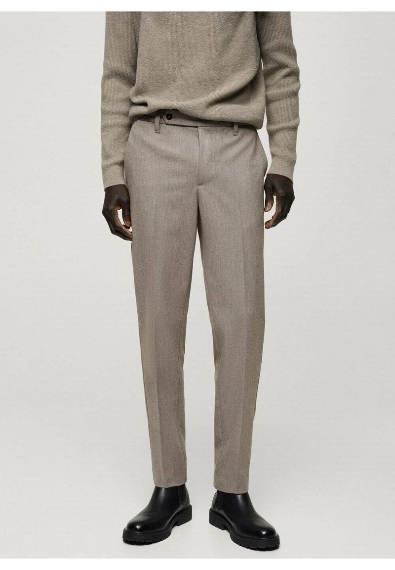 Beige op maat gemaakte broeken met een subtiele structuur, voorzien van een gladde voorkant, minimale zakken en een slim fit, gecombineerd met zwarte enkellaarsjes.