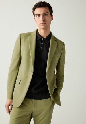 Olive green suit jacket paired with a black polo shirt. The jacket features a single button, notch lapels, and side pockets. Smooth texture.