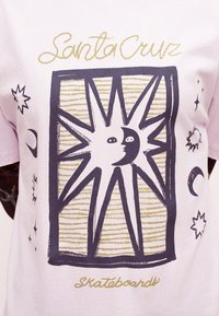 Μπλουζάκι με γραφικό ήλιο και φεγγάρι μέσα σε ορθογώνιο πλαίσιο, το κείμενο «Santa Cruz» πάνω και το κείμενο «skateboards» κάτω με χρυσή γραφή.