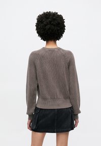 Pruun soonikootud kampsun kaelusega, pikkade pufvarrukatega ja kroogitud äärega, kombineeritud musta teksase seelikuga.