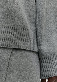 Dunkelgrauer Strickpullover und -hose im Nahaufnahme, mit gerippten Bündchen, weichem Material und überlappenden Lagen für eine lässige Passform.