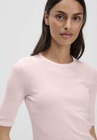 Lichtroze T-shirt met korte mouwen, gemaakt van zachte katoen. Heeft een ronde hals en een gladde, aangesloten textuur. Eenvoudig ontwerp, zonder patronen.