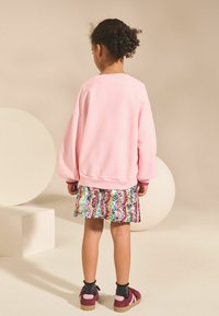 Różowy oversize'owy sweter, wielokolorowa spódnica z cekinami o falistym wzorze i bordowe buty z różowymi akcentami.