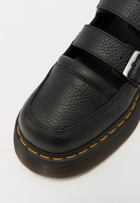 Schwarzer Lederschuh mit mehreren Riemen, strukturiertem Obermaterial und einer kontrastierenden gelben Naht entlang der Sohle. Enthält ein metallisches Schnallendetail.