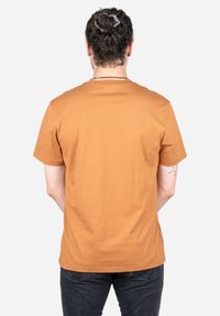 Korte mouwen t-shirt van gedempt oranje katoen, ronde halslijn, gladde textuur, geen zichtbare patronen, achteraanzicht met zwarte jeans.
