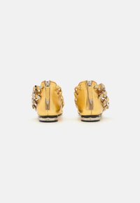 Yellow metallic booties with a smooth finish, featuring silver hardware, zippers, and braided detailing on the sides. Flat black soles.