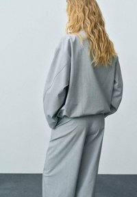 Grå oversized sweatshirt och matchande vida byxor i mjukt material, med en avslappnad passform och minimal sömdetalj.