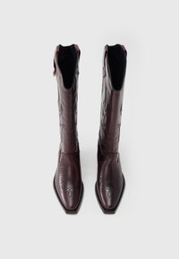 Καουμπόικες μπότες από δέρμα μπουρντό με μυτερές μύτες, περίτεχνα σχέδια ραφής και ψηλό μισό, με μαύρη σόλα και εσωτερική επένδυση.