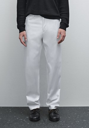 Witte broek van gladde stof, met een rechte pijpontwerp. Gecombineerd met een zwart geribd langwerpig top en zwarte veterschoenen.