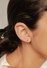 Piccola orecchino a cerchio in metallo rosa, con una superficie liscia e lucida. Indossato sull'orecchio di un modello, che mette in risalto un design minimalista.