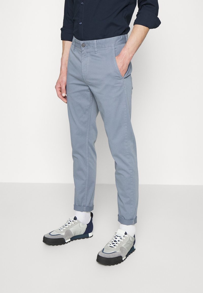 Ljusblå bomullsbukser med slim fit, med sidofickor och uppvikta benslut, tillsammans med grå och marinblå sneakers.