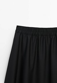 Jupe noire avec taille élastique froncée, tissu lisse et légère forme trapèze sur fond clair uni.
