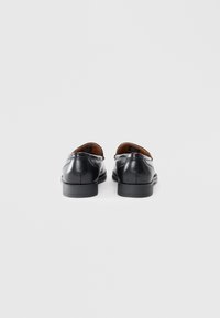 Black leather shoes with a smooth finish, rounded toe, and low heel, featuring a minimalist design and a subtle seam detail at the back.
