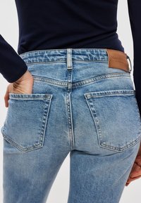 Šviesiai mėlynos spalvos derinukinės džinsinės kelnės, aptempto dizaino. Ypatingos savybės: kišenės nugaroje, odinė etiketė ant juosmens juostos ir šiek tiek sendinta tekstūra.