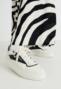 Baskets blanches et noires avec une surface texturée, présentant un panneau noir, un design à lacets et une épaisse semelle blanche.