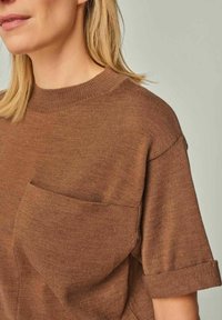 Brown short-sleeve sweater with a ribbed crew neck and a chest pocket. Soft knit texture with rolled sleeves and straight fit.