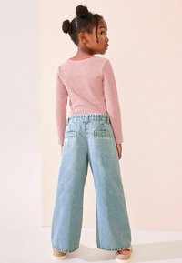 Röd- och vitrandig långärmad topp i kombination med ljusblå vida jeans. Baksidan av jeansen har två fickor och en hög midja.