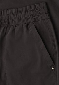 Close-up of black pants with an elastic waistband and a side pocket featuring a small metal rivet detail.