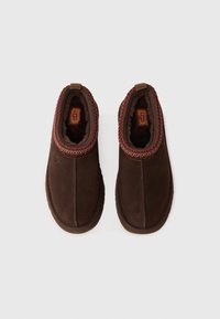 Pantoufles en suède marron, à enfiler, avec un bord tricoté rouge texturé et multicolore, dotées d'un intérieur doux et d'une semelle extérieure en caoutchouc.