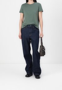 Grön bomullströja, korta ärmar, tillsammans med mörkblå vida denimjeans. Svarta skor och en mörk handväska fulländar outfiten.