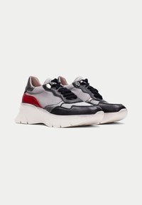 Sneakerit, joissa on harmaa ja musta nahkapinta, punaiset yksityiskohdat, paksu valkoinen pohja ja mustat nauhat. Pyöristetty kärki ja sileä pintastruktuuri.