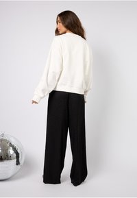 Felpa bianca oversize con polsini a costine, abbinata a pantaloni a gamba larga con stampa leopardata nera. Presenta una texture liscia e una vestibilità casual.