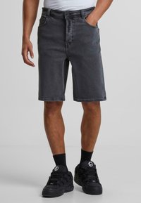 Shorts en denim gris foncé avec une coupe décontractée, featuring des passants de ceinture, des poches avant et un ourlet droit. Assortis à des baskets noires et des chaussettes.