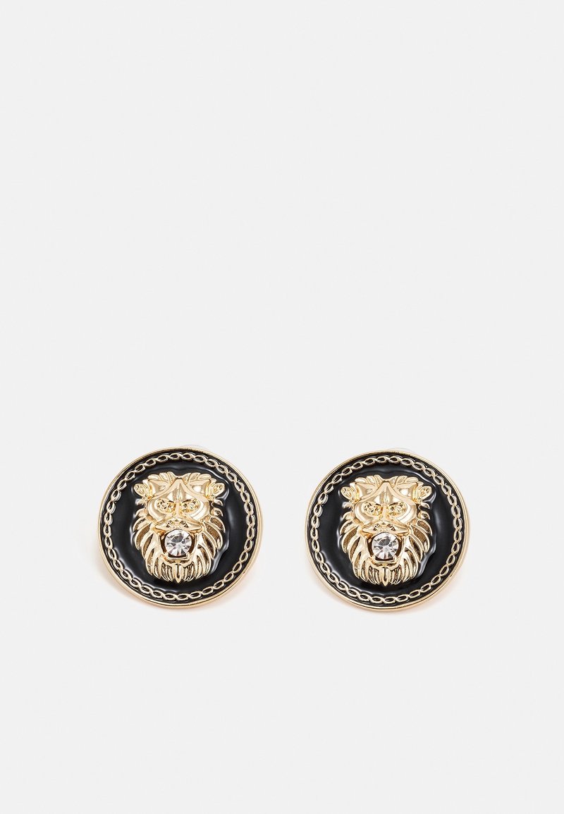 Paire de boucles d’oreilles rondes noires et dorées avec un motif en relief en forme de tête de lion et une pierre claire centrale sur chaque boucle d’oreille.