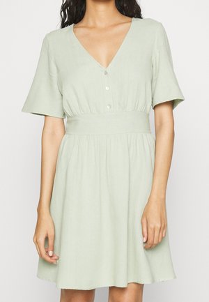 Robe verte à manches courtes avec décolleté en V, devant à boutons, taille ajustée et jupe évasée. Faite d'un tissu léger au toucher doux.