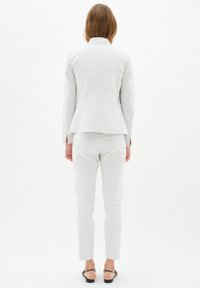 B�ílý tailored oblek, který obsahuje přiléhavý blazer s peplum pasem a úzké kalhoty. Hladká tkanina s minimalistickým designem, bez viditelných vzorů.