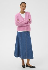 Rosa flauschige Strickjacke mit V-Ausschnitt und zwei Knöpfen, kombiniert mit einem Jeans A-Linien-Rock und schwarzen Ballerinas. Schlichtes, strukturiertes und lässiges Outfit.
