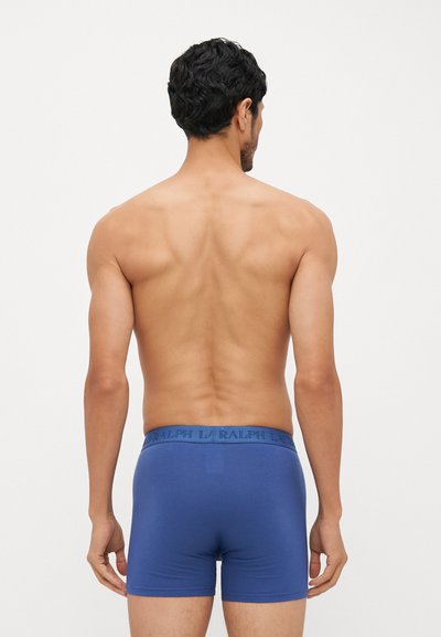 Blaue Baumwoll-Boxershorts mit einem elastischen Bund, auf dem der Markenname steht. Glatte Textur, taillierte Passform, von hinten betrachtet.