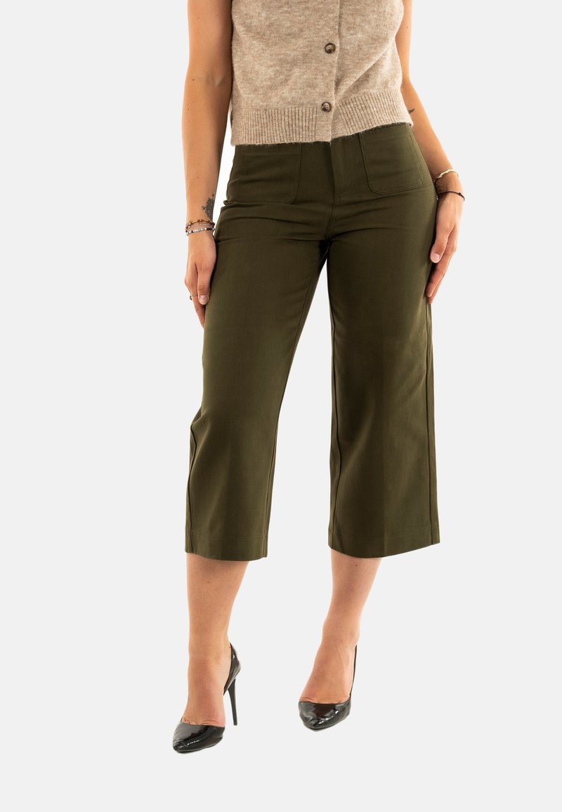 Pantalons cropped vert olive en tissu lisse avec poches avant et taille haute, associés à des escarpins noirs à bout pointu.