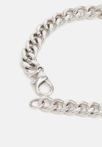 Pulseira de metal prateado em corrente com elos entrelaçados e fecho de garras. Apresenta uma superfície polida e um design robusto.